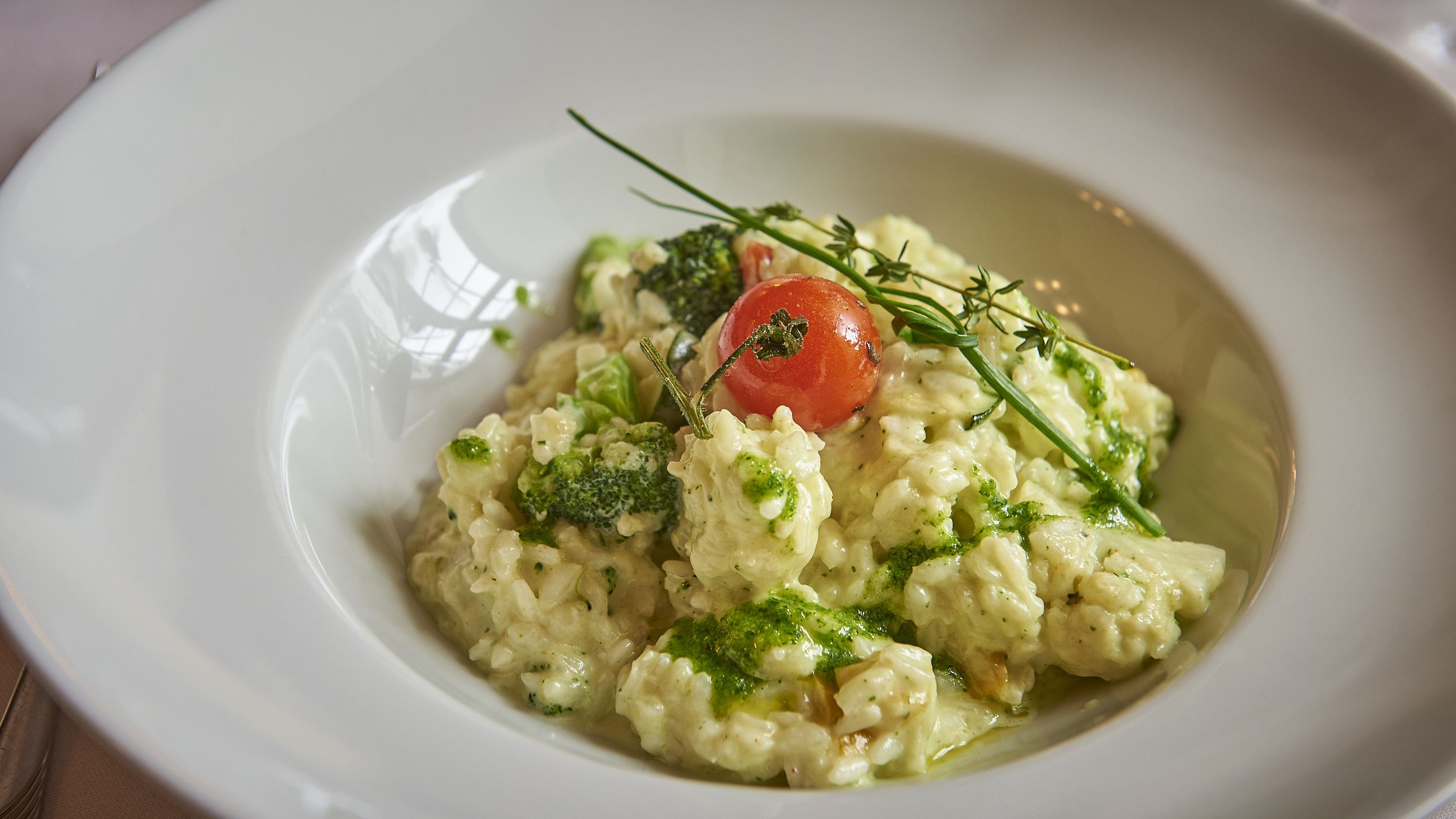 A white plate with a creamy dish garnished with broccoli, a cherry tomato, and a sprig of thyme.