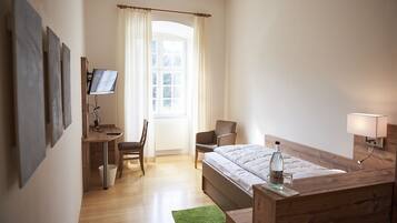 Habitación de hotel con cama, escritorio con televisor, silla y mesita de noche con lámpara.