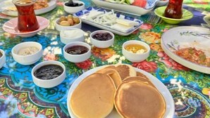 A table set with various dishes including pancakes, a pitcher of tea, and multiple small bowls of condiments. - Kavalalı Butik Otel (Cesme)