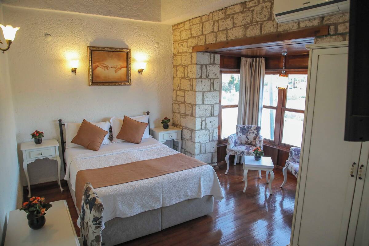 A bedroom with a large bed, a nightstand, a chair, a small table, and a wardrobe.