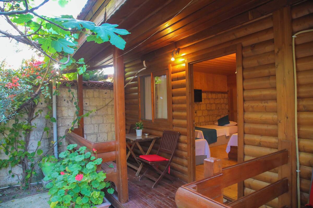 A log cabin with a wooden porch, a dining table with chairs, and a small garden area with plants and flowers.