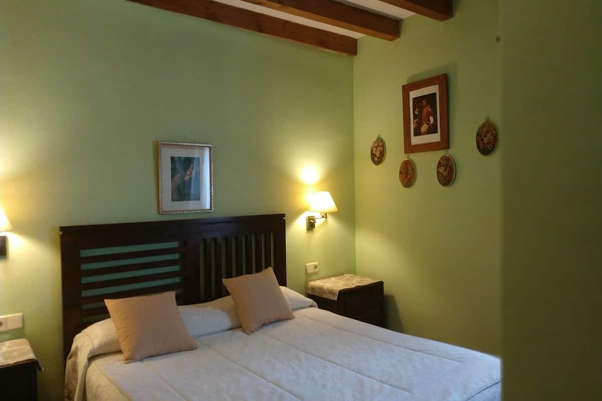 A bedroom with a bed, two bedside lamps, a wooden headboard, a framed picture on the wall, and decorative plates.