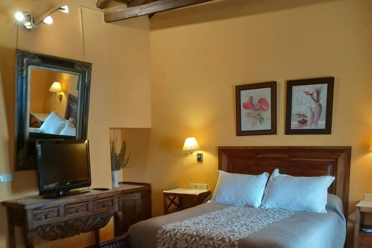 A hotel room with a bed, a desk with a television, a chair, a red sofa, and artwork on the walls.