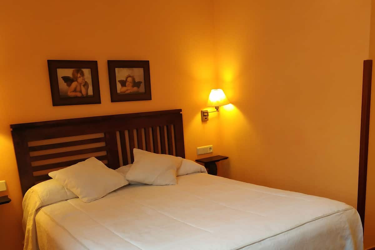 A neatly made bed with white linens in a room with orange walls and a wooden headboard.
