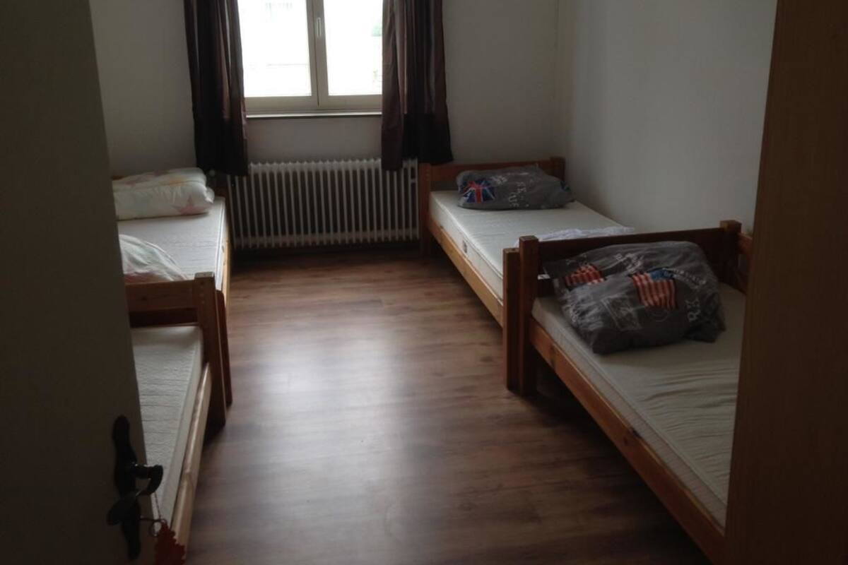 A small, dimly lit room with two wooden beds, a radiator, and a window with curtains.