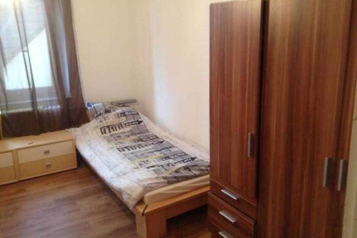 A bedroom with a bed, a wooden wardrobe, and a small bedside table.