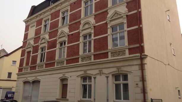 A multi-story building with red brick and cream-colored facades, featuring symmetrical window designs and decorative moldings. - Zimmer in Herne (Herne)