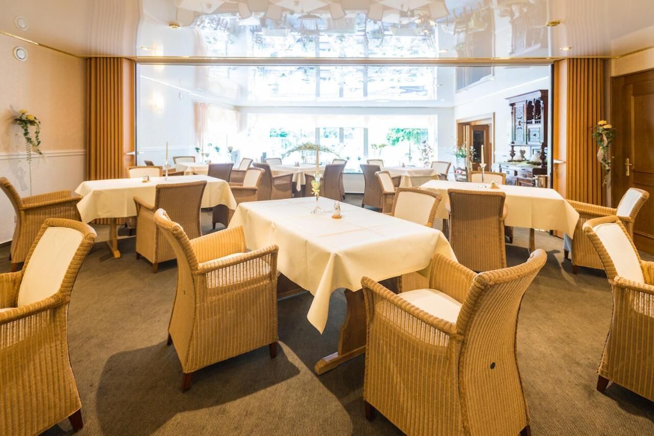 A spacious dining area with multiple tables and wicker chairs, large windows allowing natural light, and a modern ceiling design.