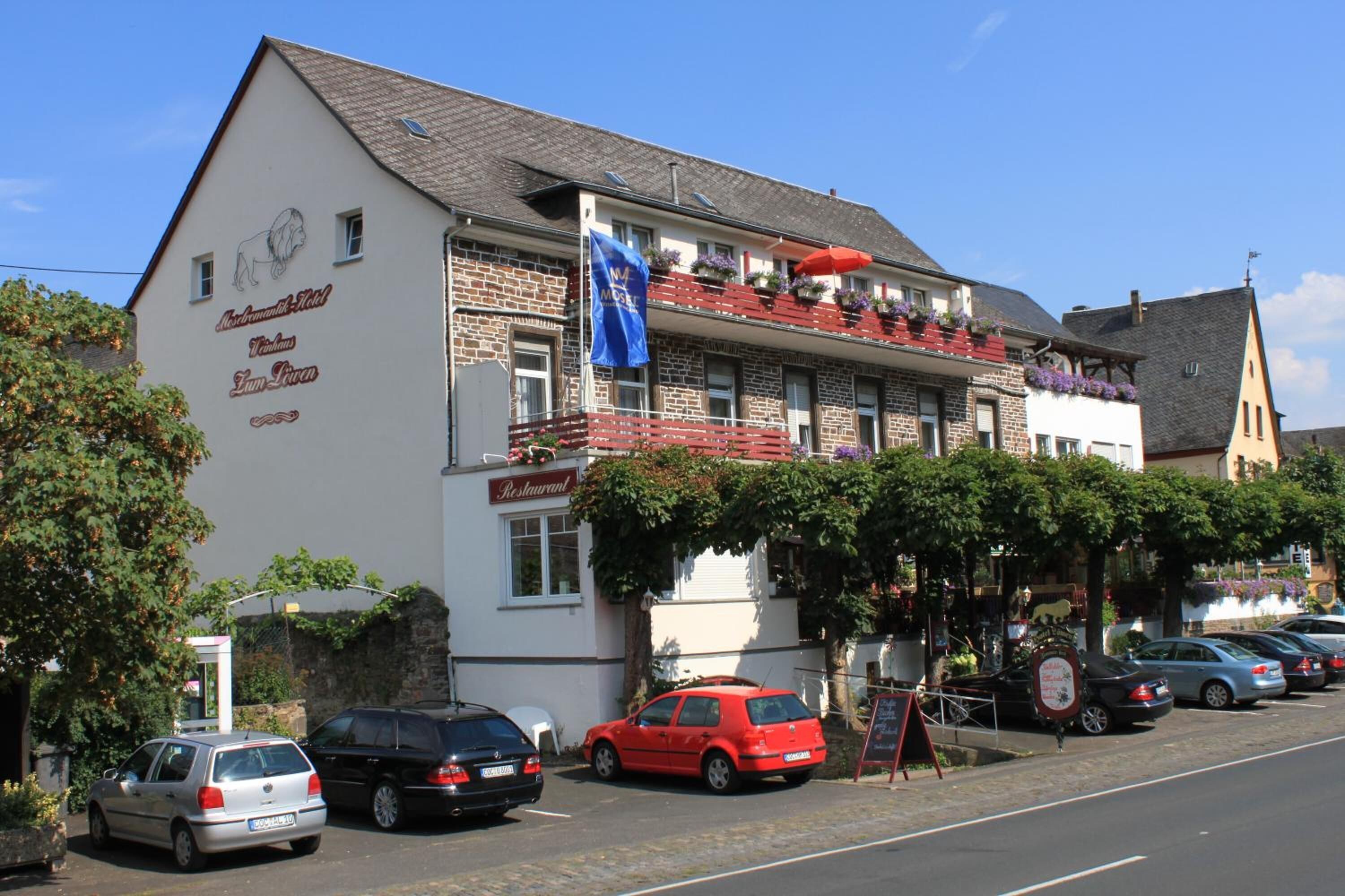 Un edificio con un letrero de restaurante, una bandera y coches estacionados.