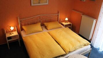 Una cama individual con ropa de cama amarilla, dos mesitas de noche con lámparas, un radiador y un cuadro en la pared.