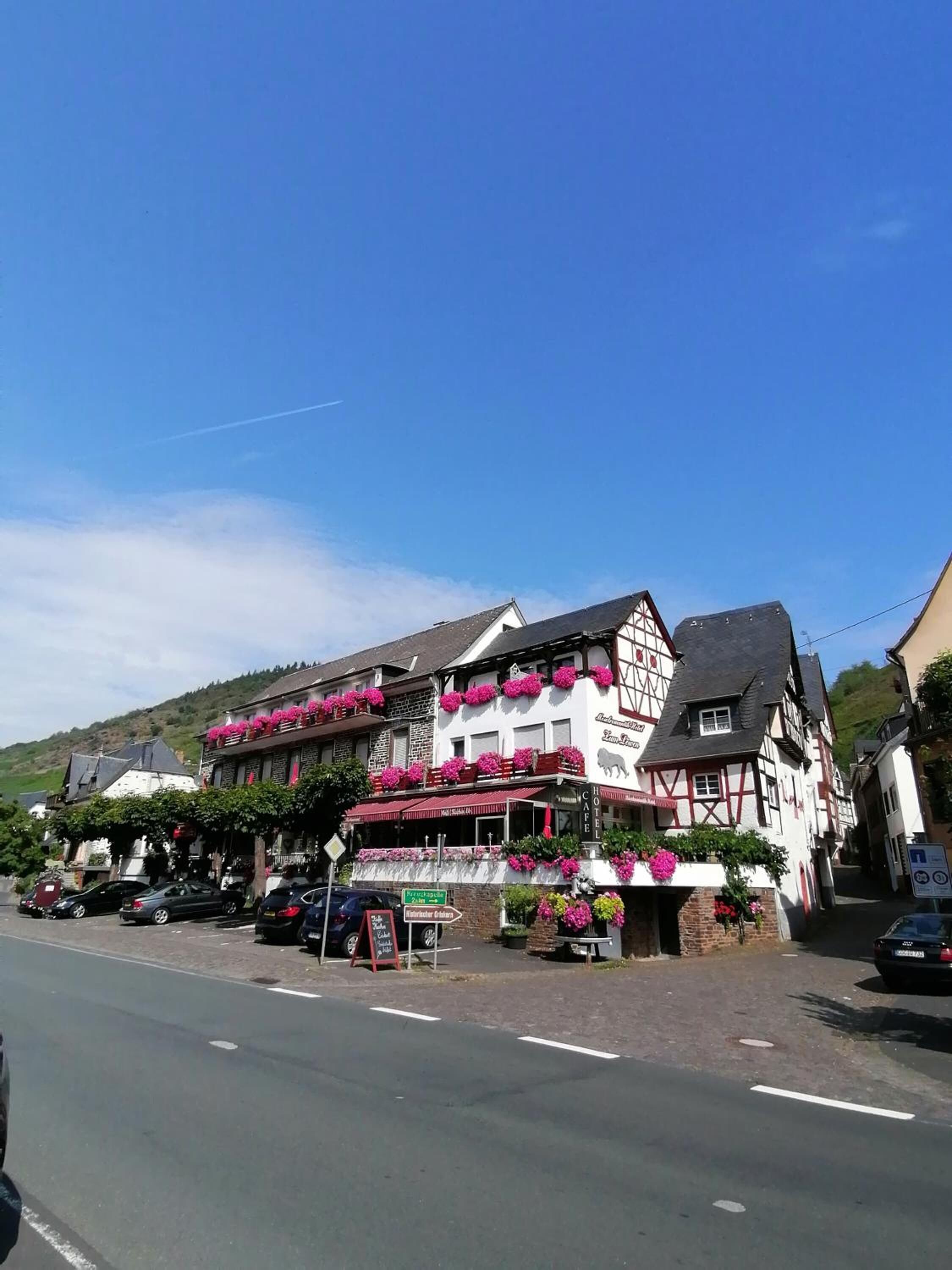 A traditional half-timbered building with a café on the ground floor, surrounded by parked cars and a clear blue sky.