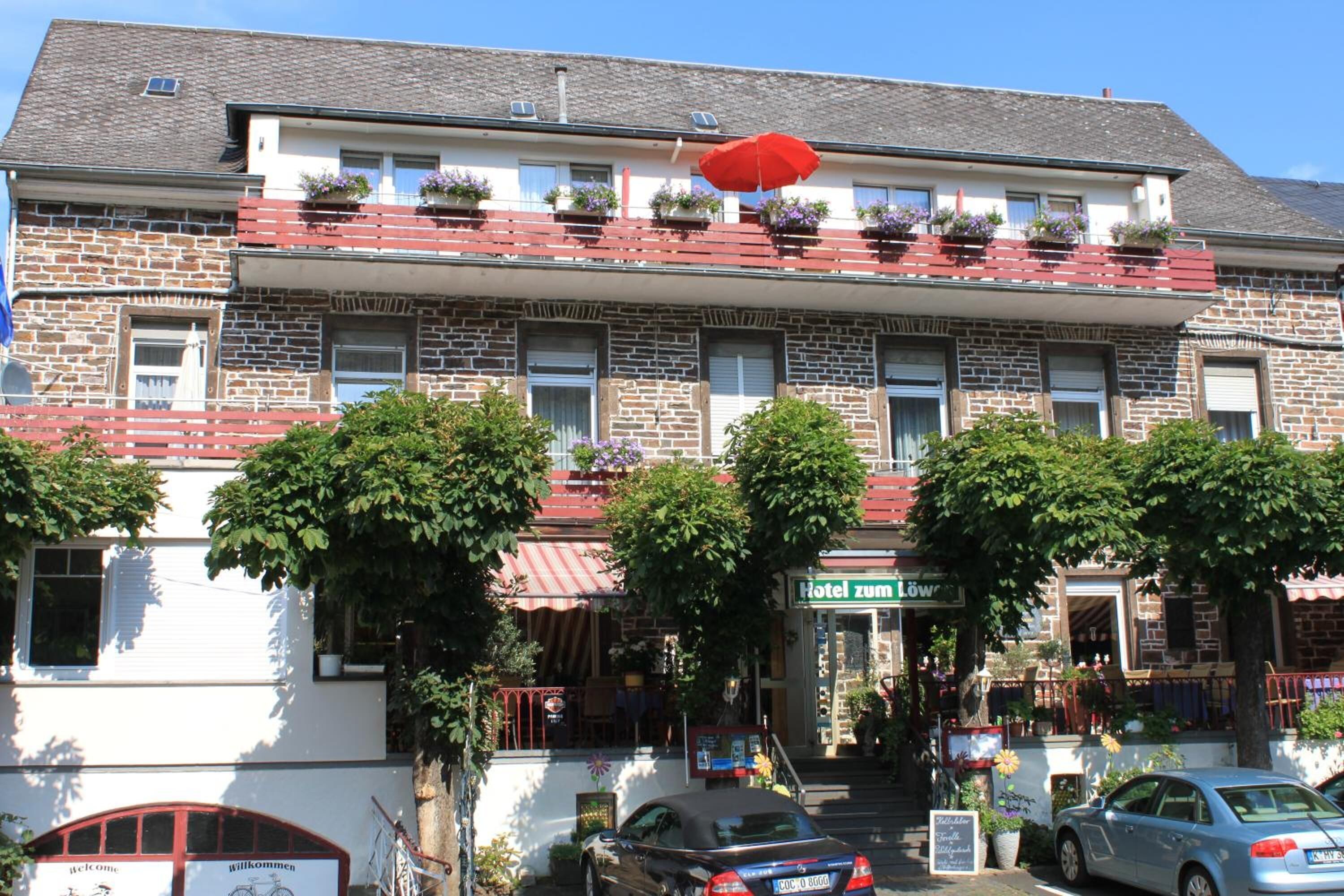Un hotel amb façana de pedra, balcons vermells amb jardineres florals i un rètol que diu "Hotel zum Löw".