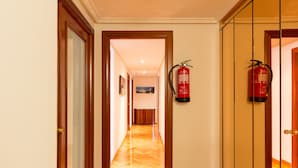 Un pasillo de hotel con puertas de madera, un extintor de incendios en la pared y suelo de madera.