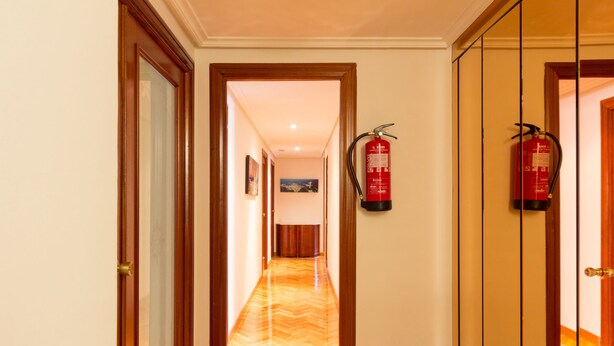 A hotel hallway with wooden doors, a fire extinguisher mounted on the wall, and a wooden floor. - Pensión La Rioja (Logroño)