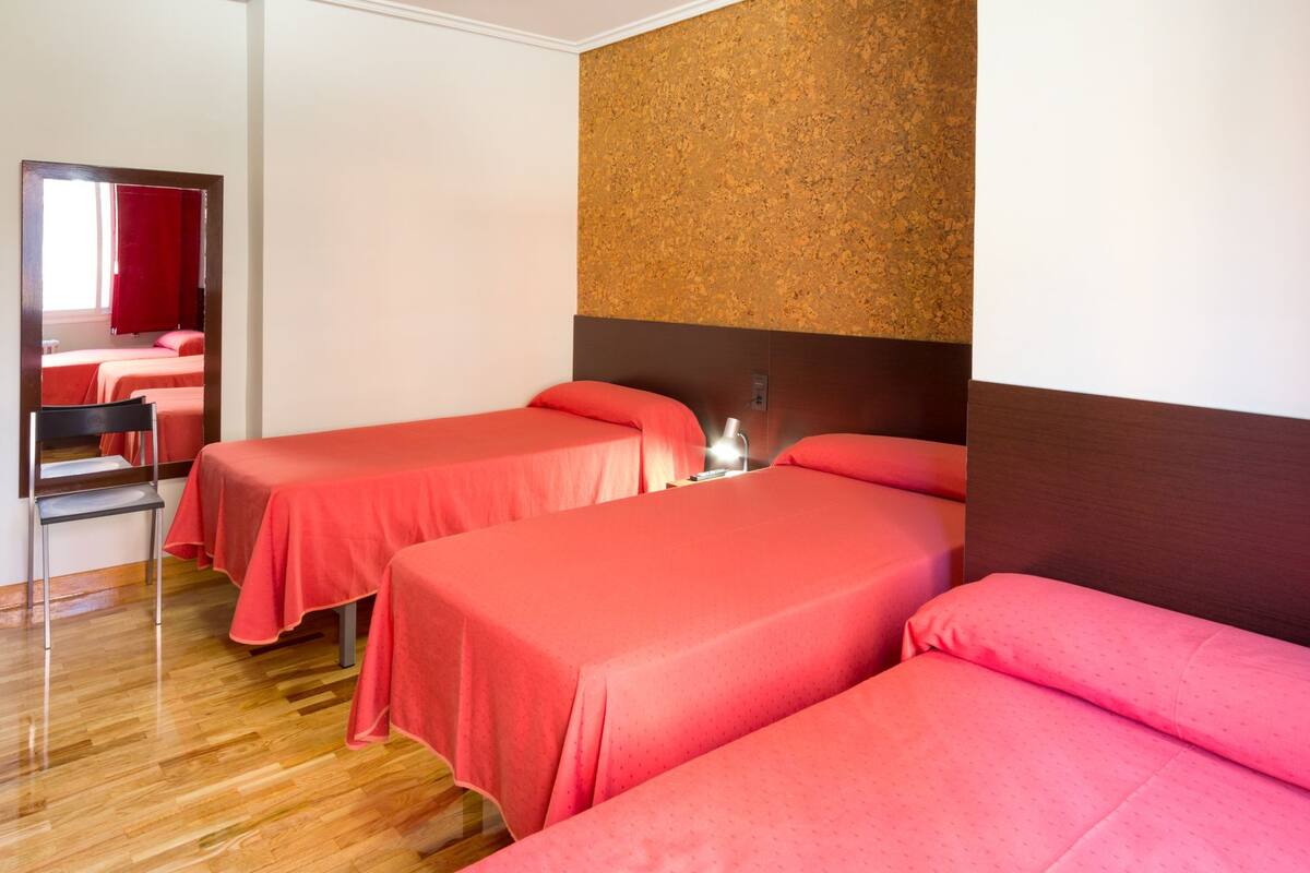 A hotel room with two single beds, a wooden floor, a mirror, and a cork wall.