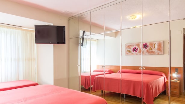 Habitación de hotel con dos camas, un televisor montado en la pared y un cuadro sobre las camas.