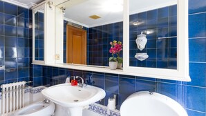 Un baño con azulejos azules, un lavamanos blanco, un inodoro y un espejo.