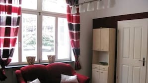 Ein Zimmer mit einer roten Couch, weißen Vorhängen, einem Fenster mit Blick, einer weißen Tür und einem Schrank.