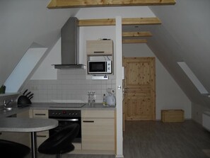 A compact kitchen with a microwave, stove, and wooden cabinets. - Ferienwohnung am Kamp (Bad Doberan)