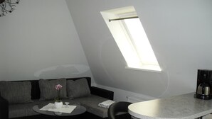 A compact living space with a sofa, a small round table, a coffee machine, and a skylight. - Ferienwohnung am Kamp (Bad Doberan)