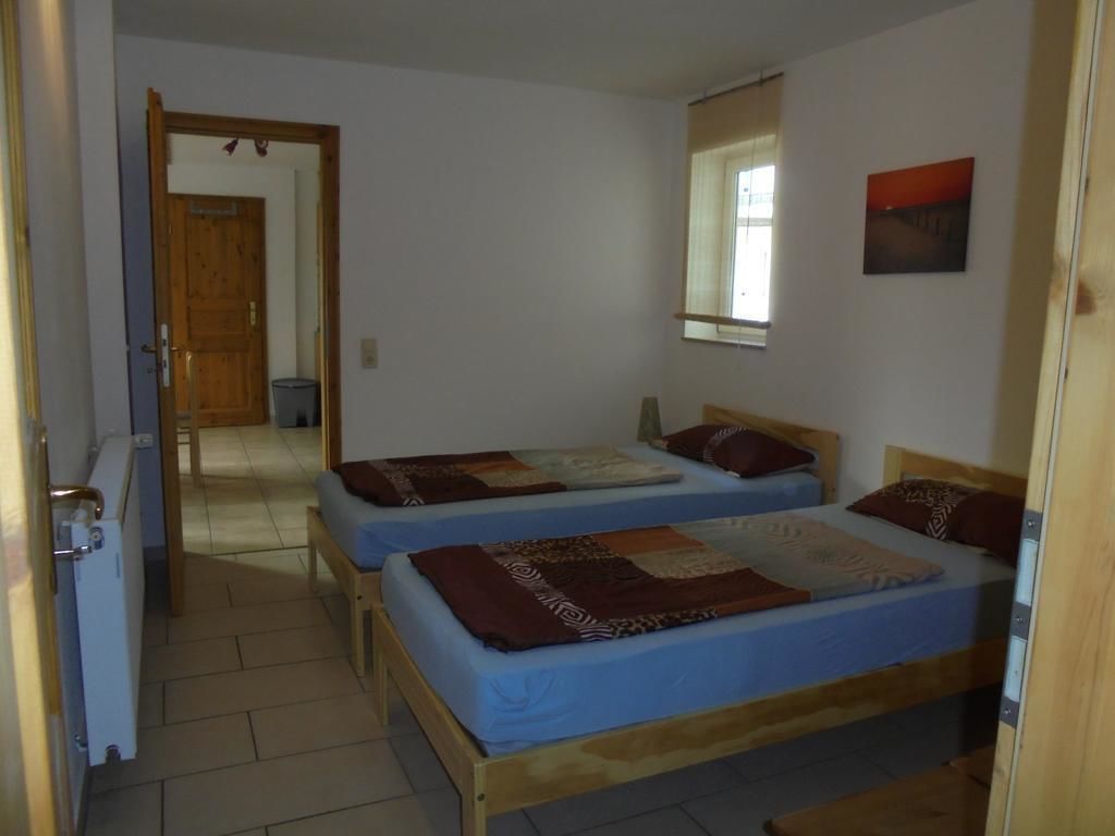 Una habitación con dos camas de madera, un ventanal pequeño y una puerta que da a otra estancia.