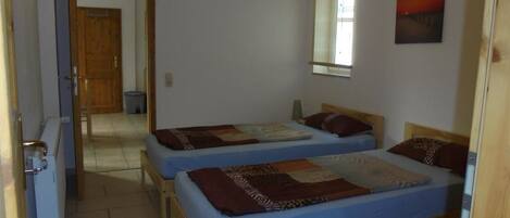 Una habitación con dos camas de madera, un ventanal pequeño y una puerta que da a otra estancia.
