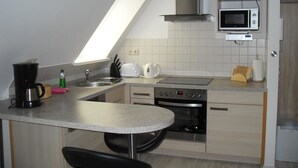 A compact kitchen with a microwave, stove, and sink. - Ferienwohnung am Kamp (Bad Doberan)