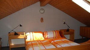 A cozy attic bedroom with a wooden bed, two bedside lamps, and a small wall decoration. - Herrmanns - Ferienhaus (Zandt)