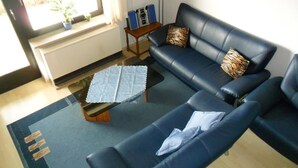 A living room with a blue sofa, a coffee table, and a small side table with books and speakers. - Herrmanns - Ferienhaus (Zandt)
