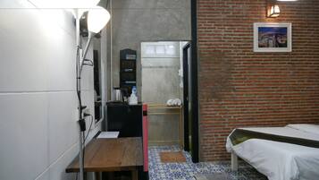 Camera d'albergo compatta con un letto, un tavolino, un lavandino e uno specchio. Si vede un muro in mattoni e una finestra con vista.
