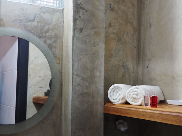 A bathroom with a wooden shelf holding rolled towels and two bottles. - Nature Park Resort (Phitsanulok)