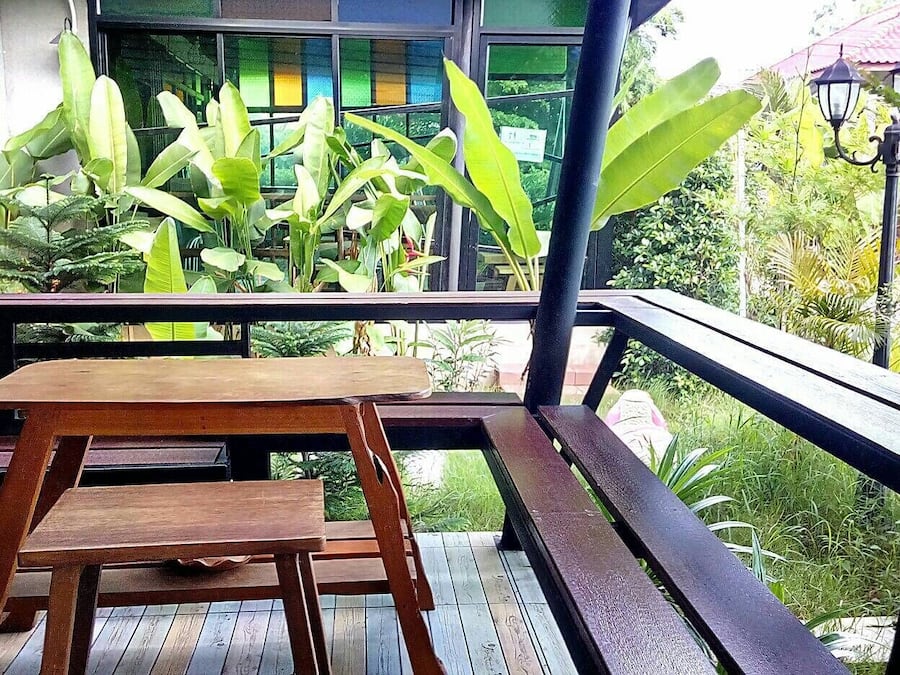 A wooden table and bench on a balcony with a view of lush greenery and a building with large windows.