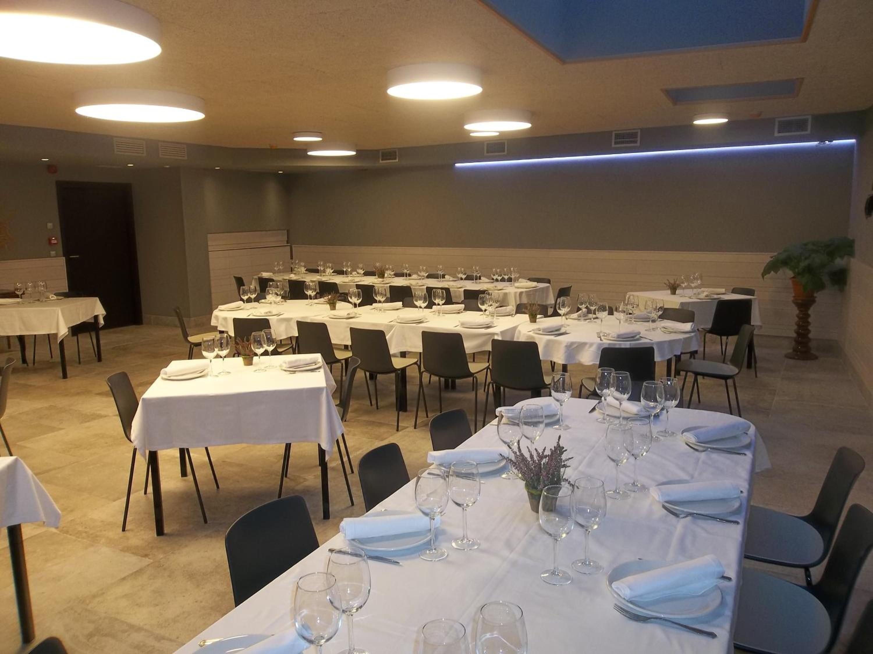 A banquet hall with multiple round tables set for dining, each with white tablecloths, chairs, and glassware.