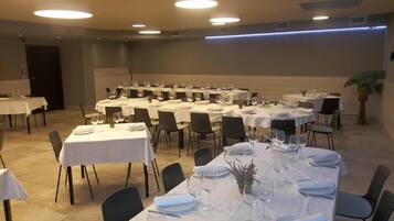 A banquet hall with multiple round tables set for dining, each with white tablecloths, chairs, and glassware.