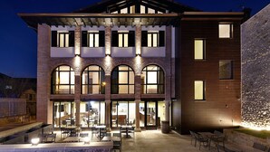 Un edificio de varios pisos con grandes ventanales y un patio con mesas y sillas al aire libre.
