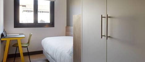 A bedroom with a bed, a desk, a chair, and a wardrobe.