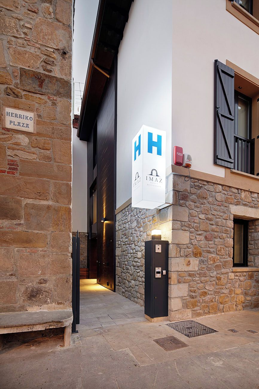 L’entrée d’un hôtel, avec une façade en pierre, une enseigne indiquant « HERRIKO PLAZA » et un panneau en forme de « H » qui indique le nom de l’hôtel.