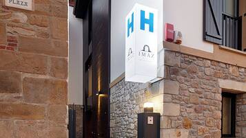 L’entrée d’un hôtel, avec une façade en pierre, une enseigne indiquant « HERRIKO PLAZA » et un panneau en forme de « H » qui indique le nom de l’hôtel.