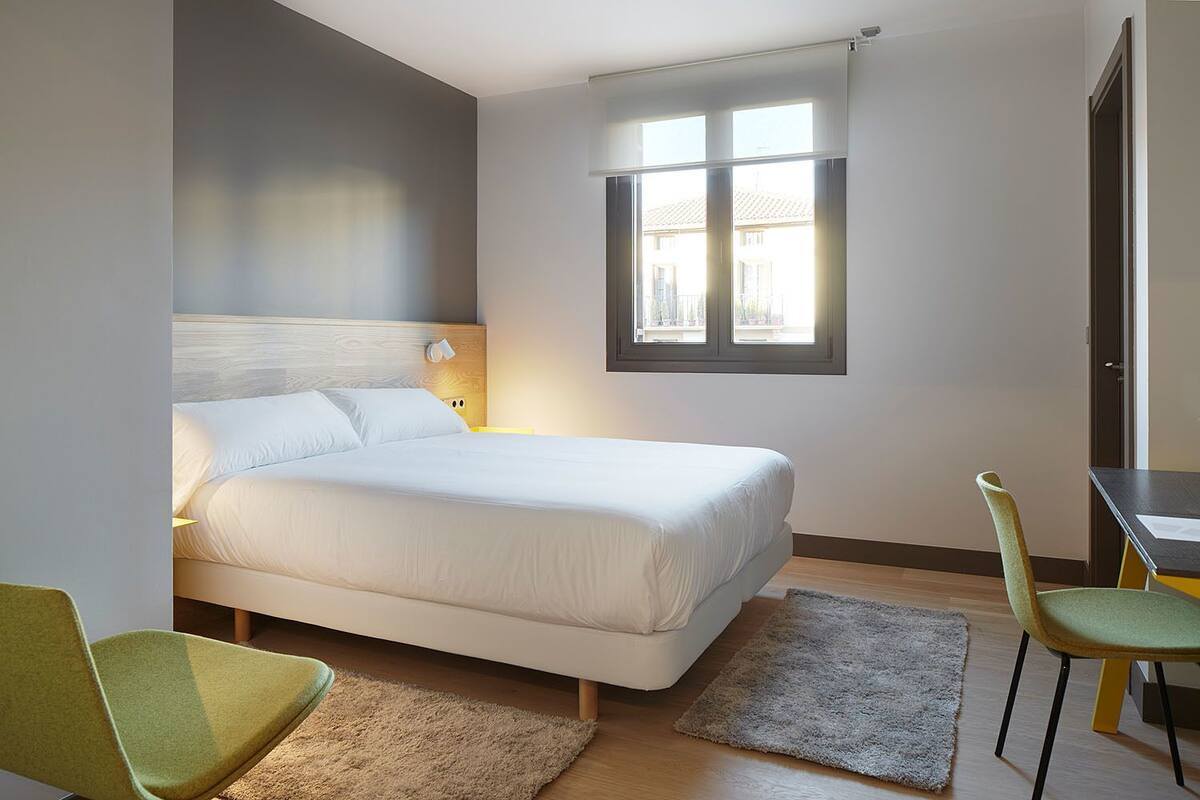 Ein Schlafzimmer mit einem Bett, einem Schreibtisch, zwei Stühlen, einem Fenster und einem Nachttisch.