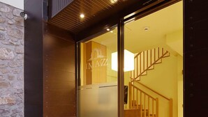 Una entrada moderna a un edificio con puerta de vidrio, escalera de madera y pared de piedra.
