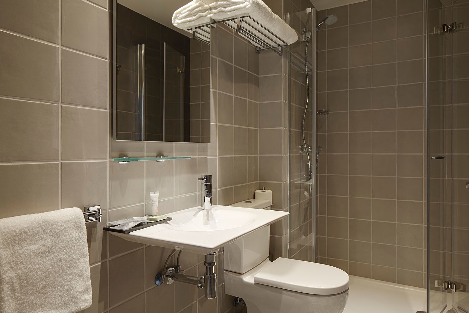 Ein modernes Badezimmer mit einem weißen Waschbecken, einer Toilette, einer Duschkabine aus Glas und einem Spiegel über dem Waschbecken.