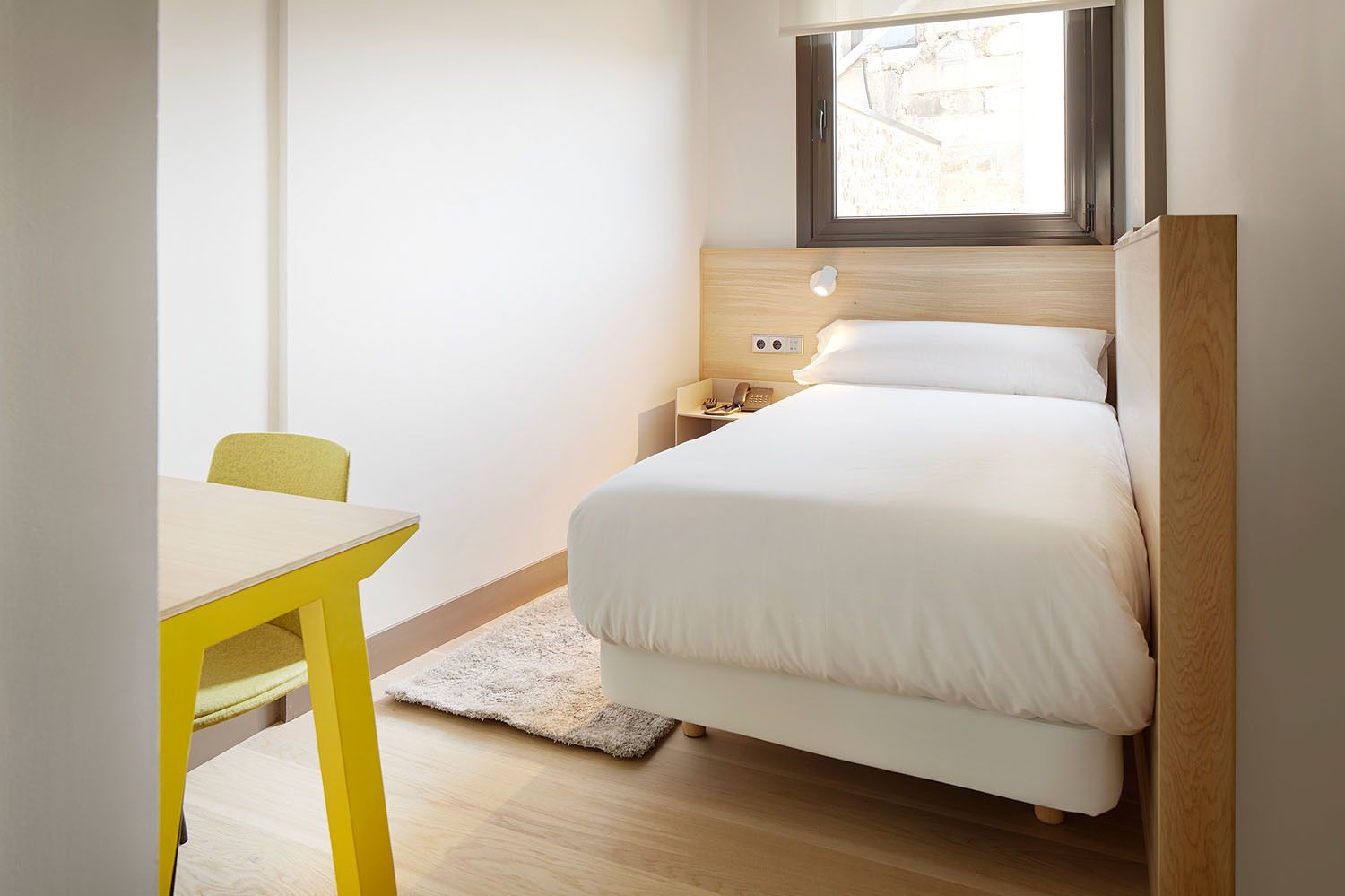 A bedroom with a bed, bedside table, and a window.