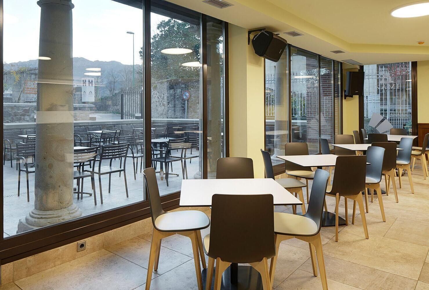 Un restaurante con amplios ventanales, mesas y sillas dispuestas para comer.