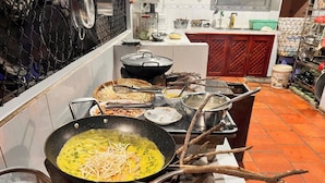 Una cocina con un wok sobre fuego abierto, cocinando alimentos. Se observan diversos utensilios y ingredientes.