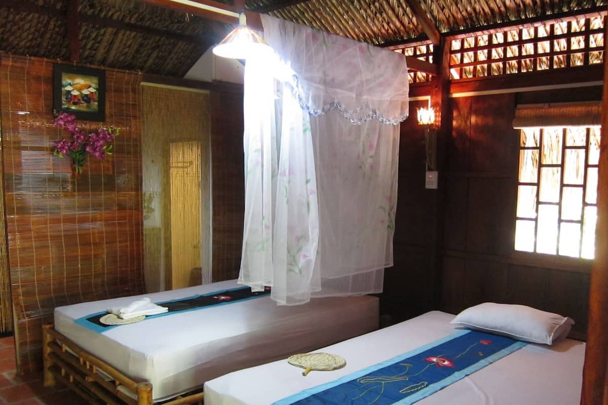 Una habitación con dos camas, mosquitero y ventana con celosía de madera.