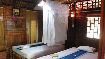 A room with two beds, a mosquito net, and a window with a wooden lattice.