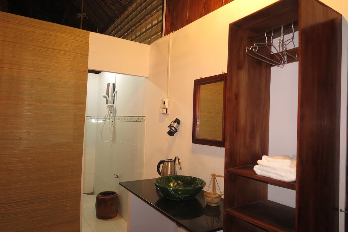 Un baño con tocador de madera, un lavamanos de cerámica verde, un perchero y una zona de ducha.