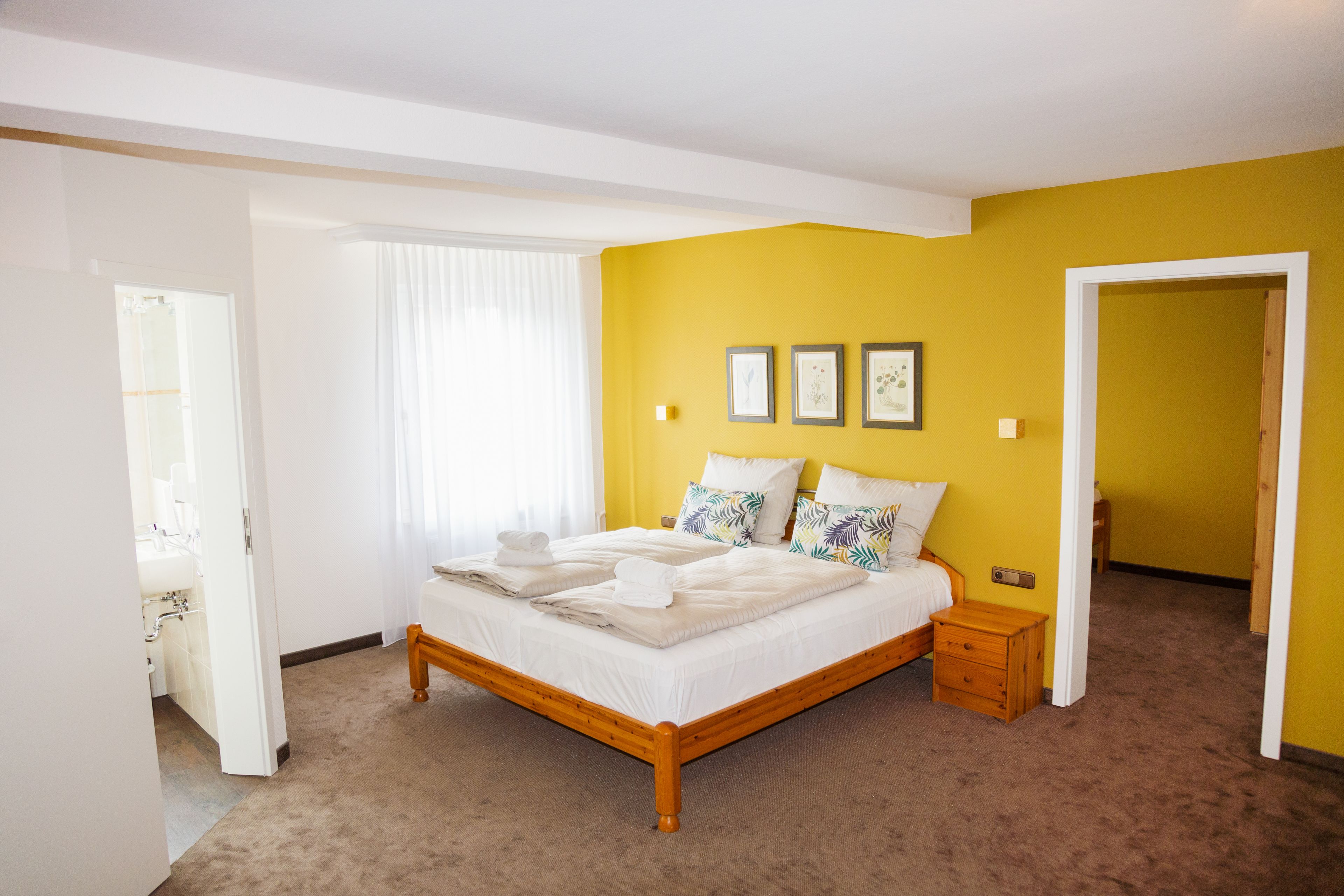 Un dormitorio con una cama de madera, ropa de cama blanca y una pared de acento amarilla.