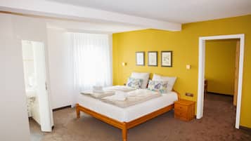 Ein Schlafzimmer mit einem hölzernen Bett, weißer Bettwäsche und einer gelben Akzentwand.