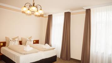 A hotel room with a large bed, two bedside tables, a chandelier, and a window with curtains.